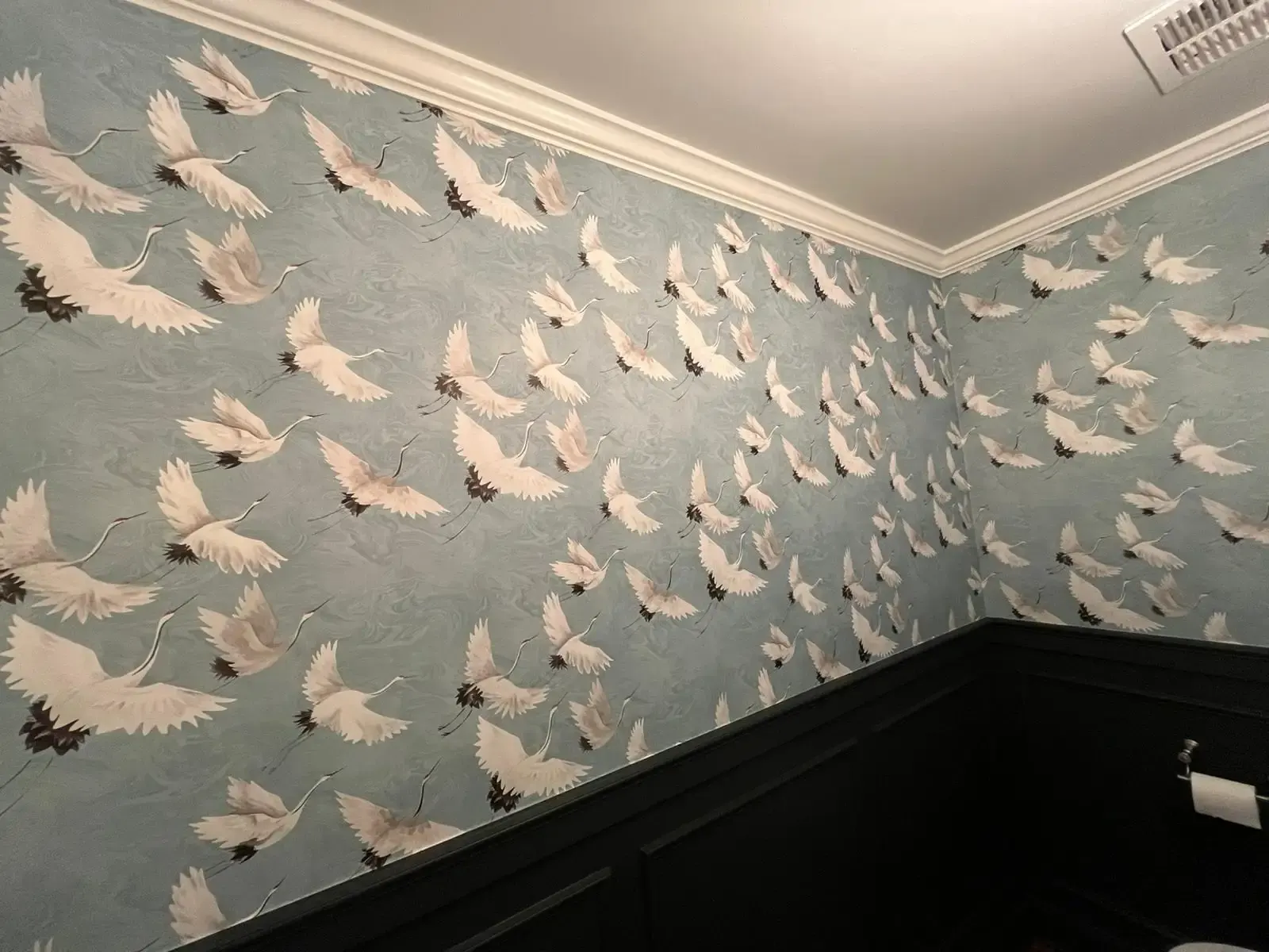 Wallpaper with flying cranes on a pale blue ground above dark painted wainscoting