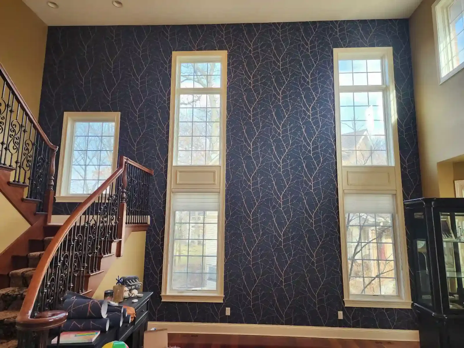 Navy wallpaper with fine gold branches on a tall stair-hall wall between narrow windows