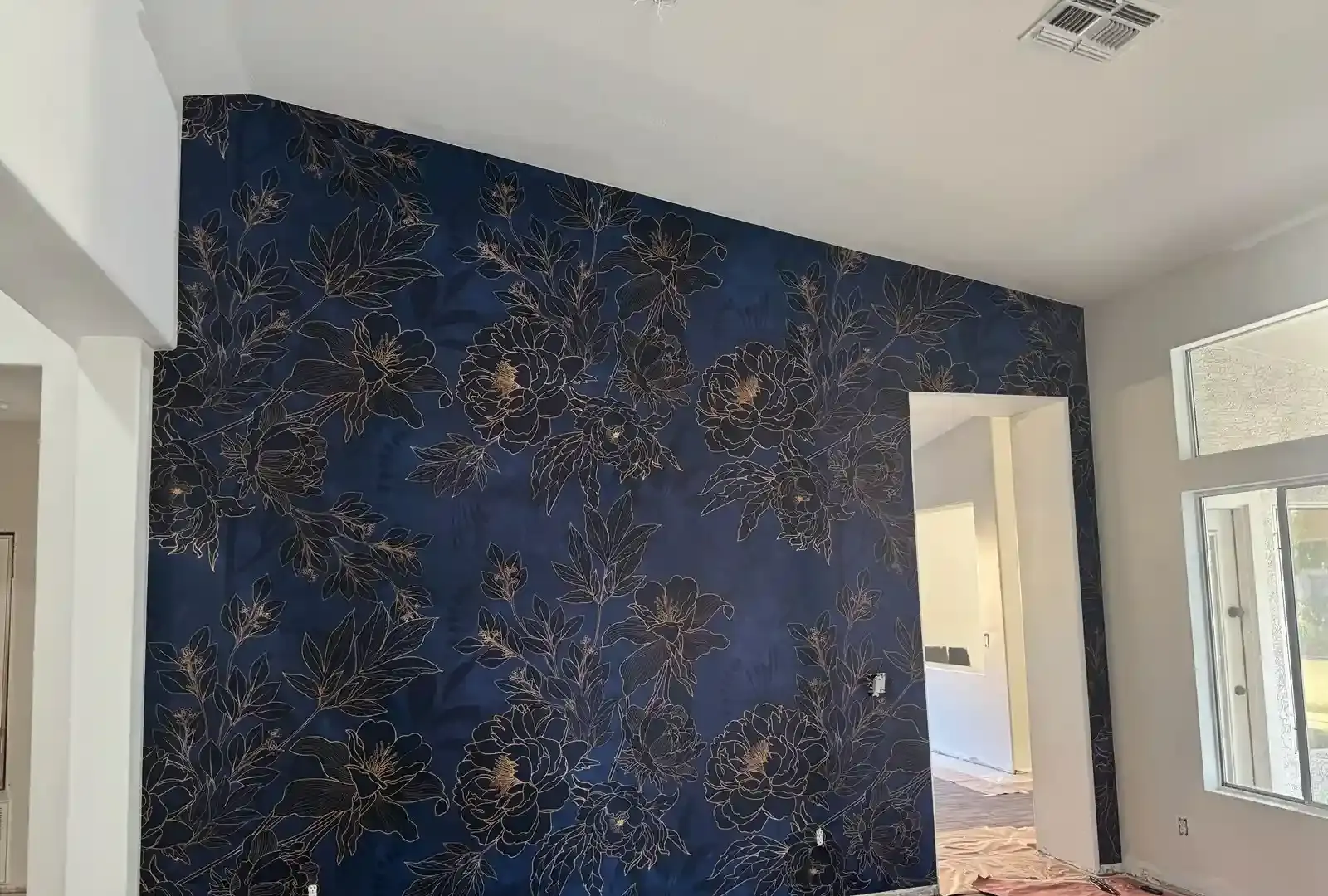 Accent wall covered in deep navy wallpaper with fine gold floral outlines